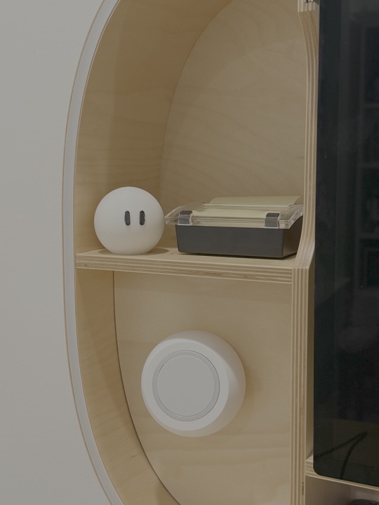 The printed Grok Bot on a plywood shelf, slightly farther back, eyes slanted.